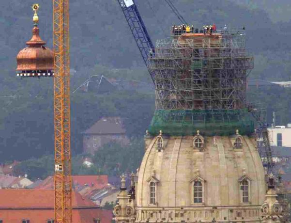 O macara ridică cupola de cupru și crucea de aur la vârful reconstruitului Frauenkirche din Dresda, Germania