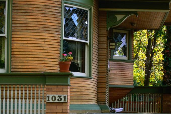 Detaliu de pridvor de casă rotunjită, paravane din lemn natural cu ornamente verzi, ferestre cu plumb dublu atârnate, panglici decorative