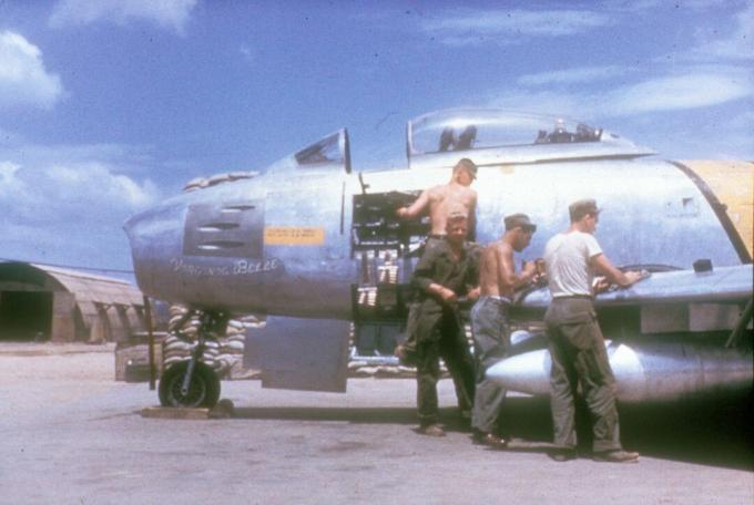 Armurere alături de un Sabre F-86 cu un panou lateral scos.