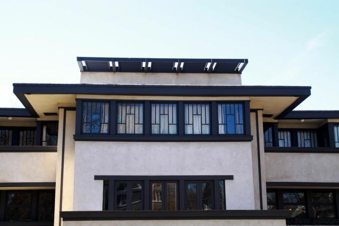 casă laterală orientată pe orizontală, cu bordură maro închis, acoperiș plat cu suprafețe uriașe și rânduri de ferestre cu sticlă cu plumb