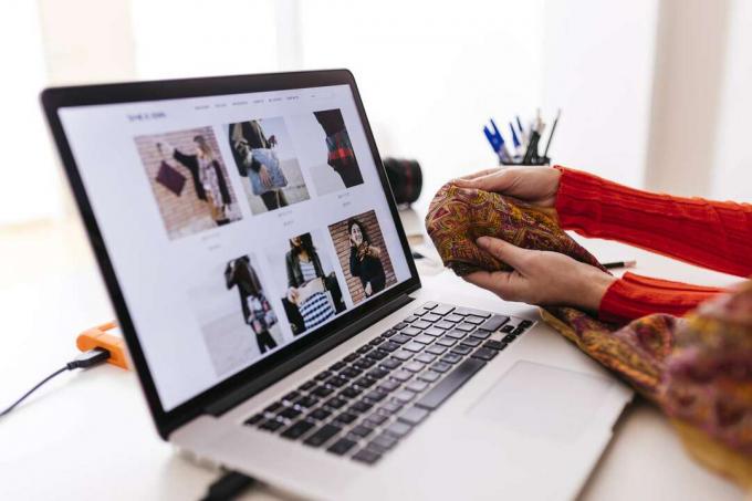 Femeie care ține țesătura în fața unui laptop cu un site web de modă deschis
