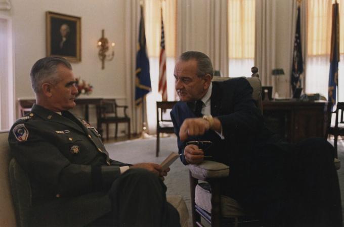 Generalul William Westmoreland, în uniforma armatei americane și așezat, vorbește cu președintele Lyndon B. Johnson în Oval Office.