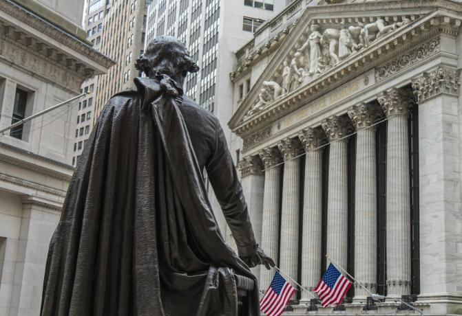 O statuie a lui George Washington privește spre clădirea Bursei din New York pe Broad Street de la Federal Hall National Memorial de pe Wall Street din New York.
