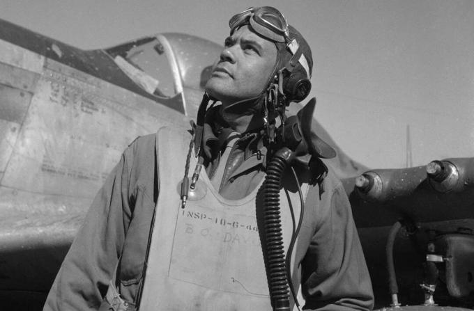 Benjamin O. Davis într-un costum de zbor și cască stând în fața unui luptător Mustang P-51.